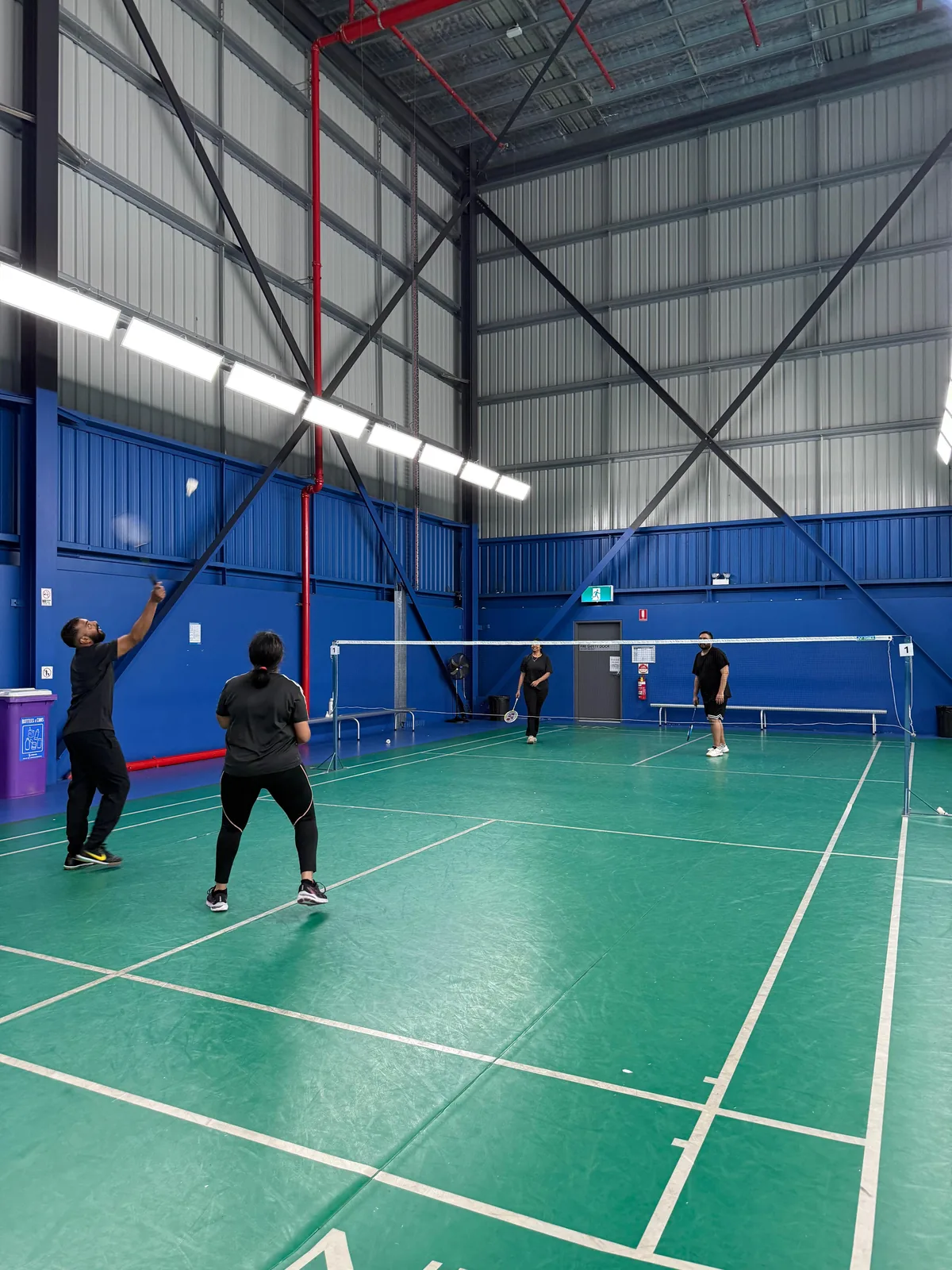 Four players mid-rally in a badminton doubles match