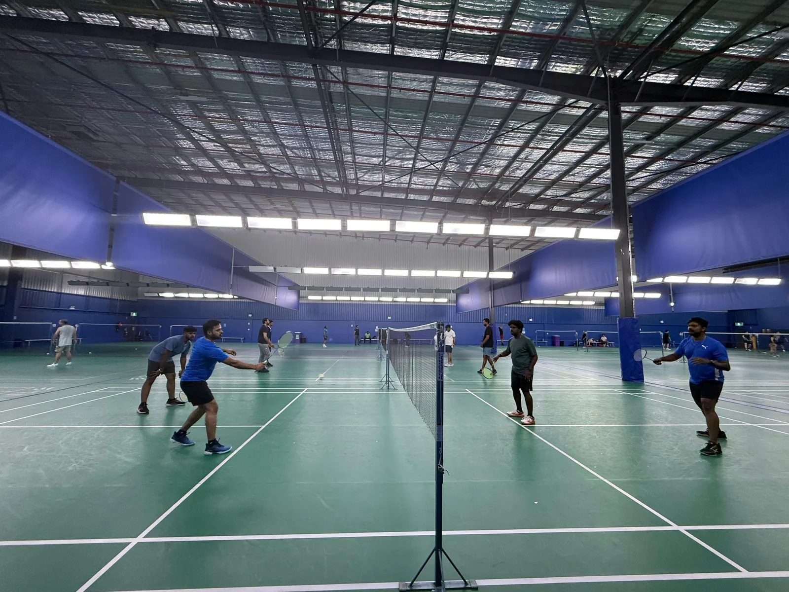 Busy indoor badminton hall with several courts in play