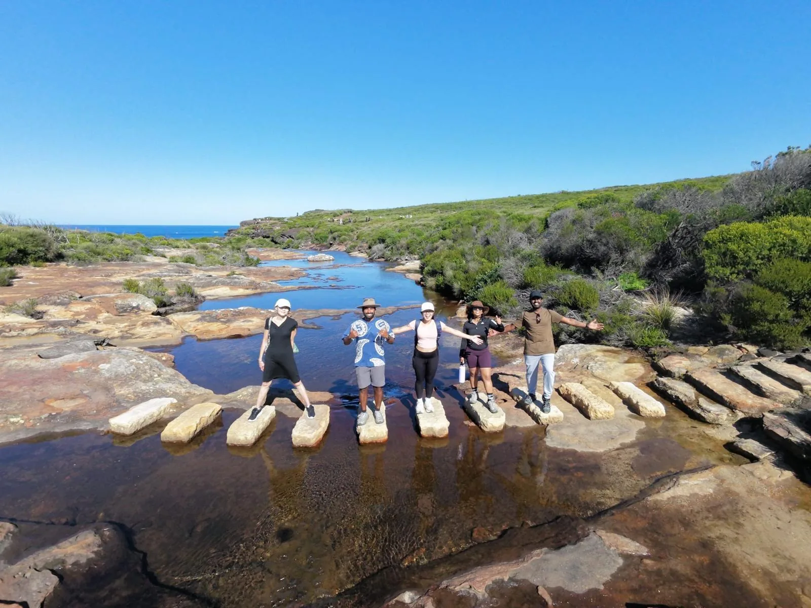 Hikers posing on coastal stepping stones under a clear sky